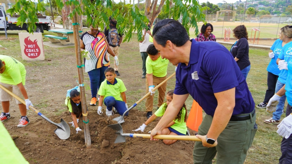 children and adults with shovels putting dirt in a newly planted tree