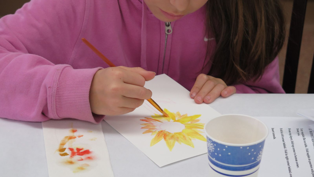 child in pink zip up hoodie watercoloring with yellow paint