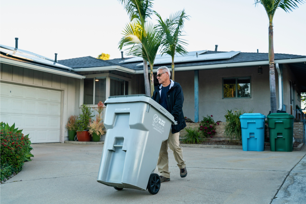 man taking his gray bin to the curb