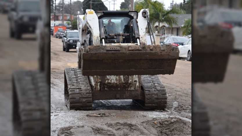 City worker in a bulldozer cleaning up mud on a street
