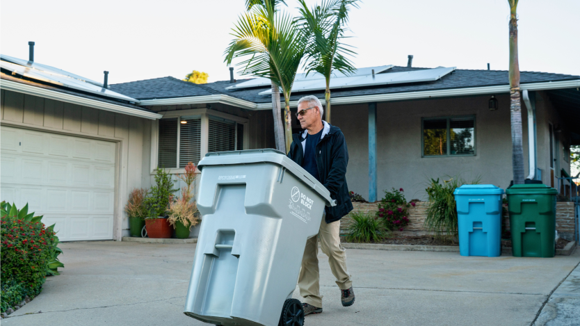 Man pushing his gray bin to the curb in front of his house.