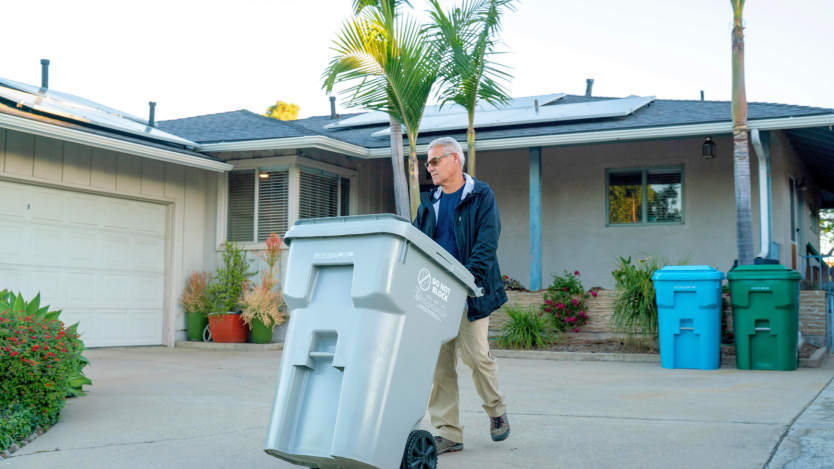 Man rolling out gray bin to the curbside