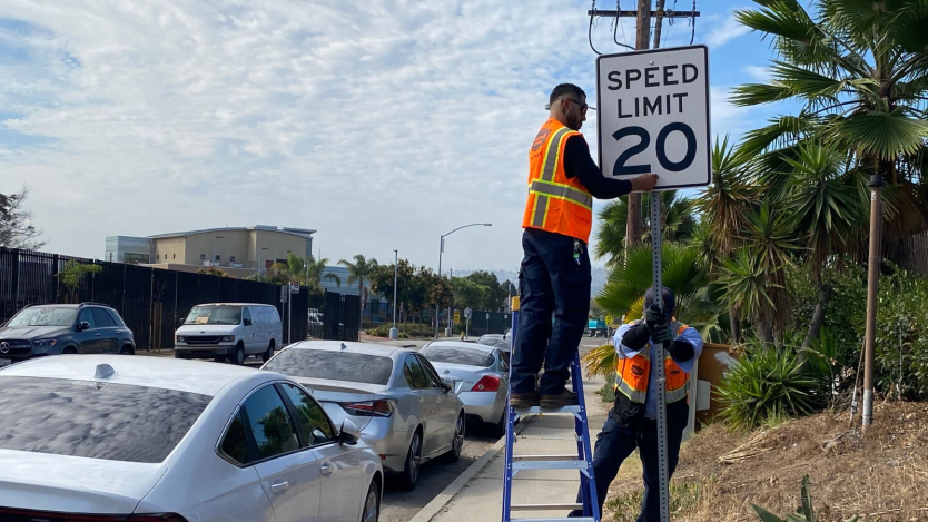 2 city workers installing a 20 mph speed limit sign.