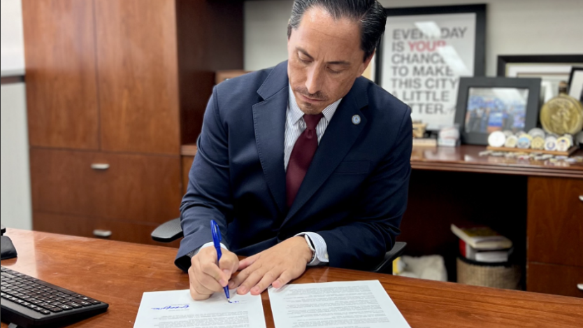 Mayor Todd Gloria sitting at his desk with a paper and pen.